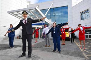 Airline staff and pilot pose with arms out for Project Wingman run by NHS volunteers and trained by Optima UK